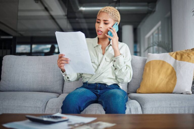 Femme assise dans un canapé, téléphone à l'oreille, examinant sa facture avant de changer de forfait mobile