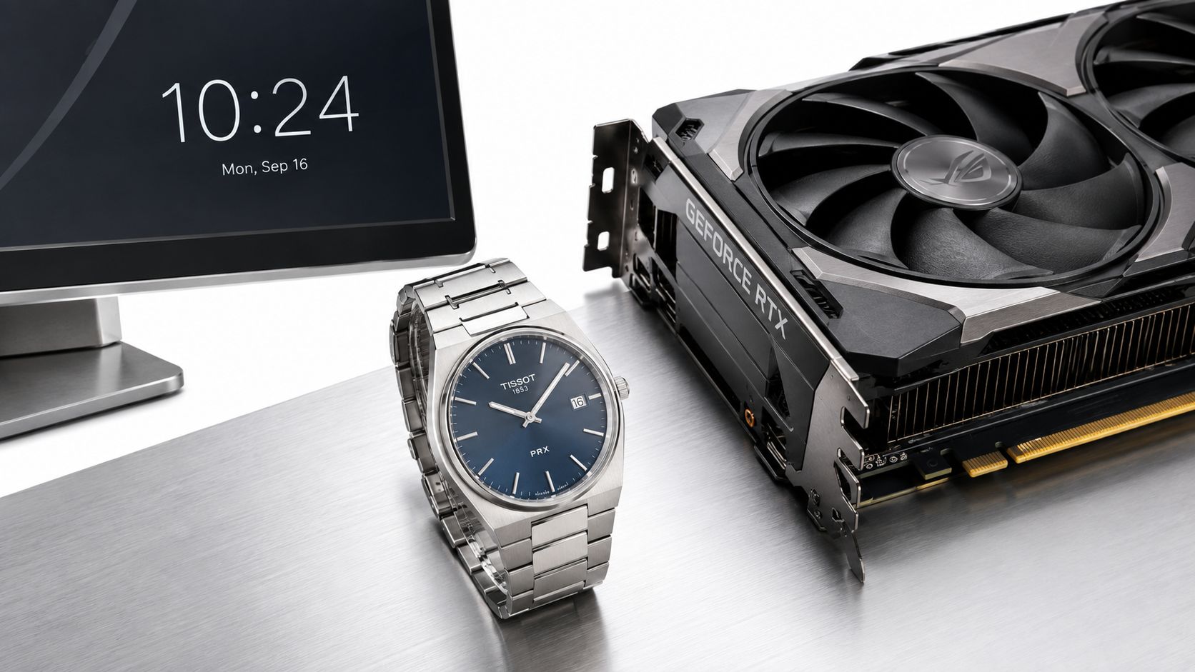A silver Tissot PRX watch with a blue dial sits beside a gaming graphics card and monitor.
